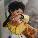 childing hugging a teddy bear and hiding mouth