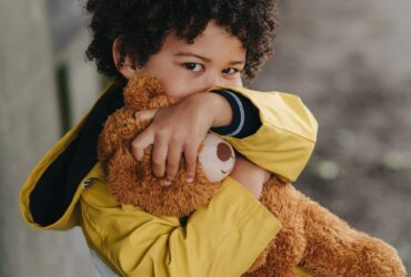childing hugging a teddy bear and hiding mouth